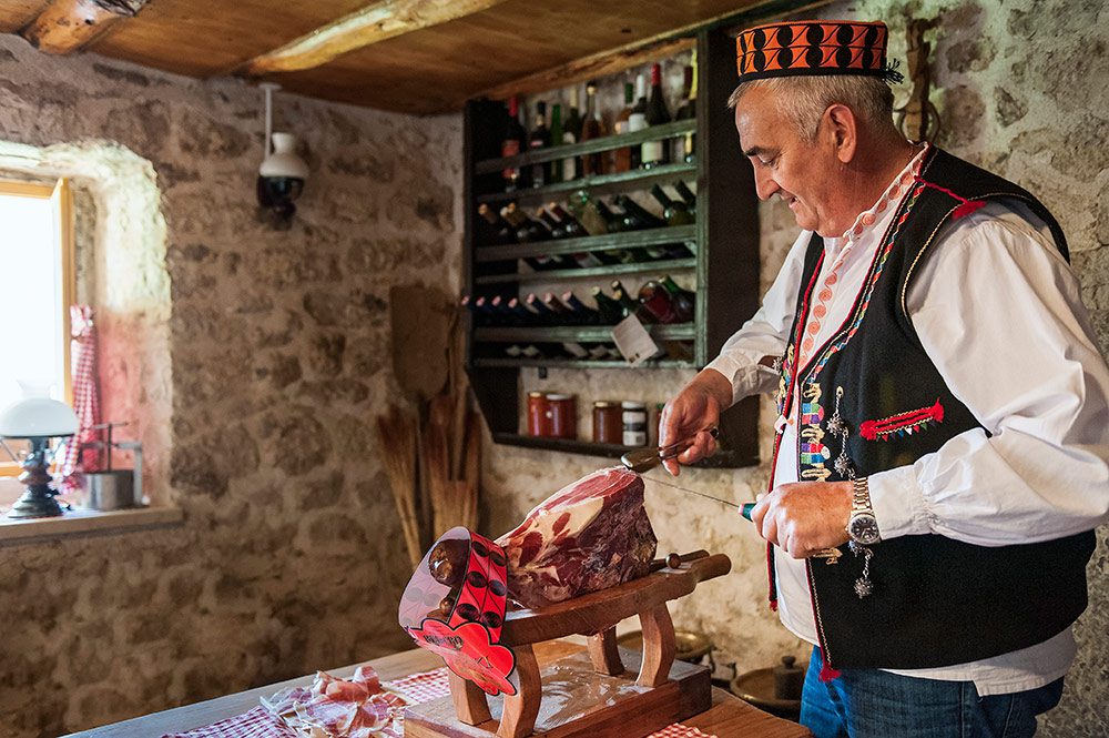 Man in traditional clothes slicing cured ham in a rustic kitchen